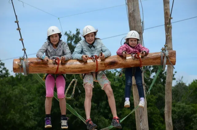 Children on a suspended log obstacle wearing helmets and harnesses at Glavani Park